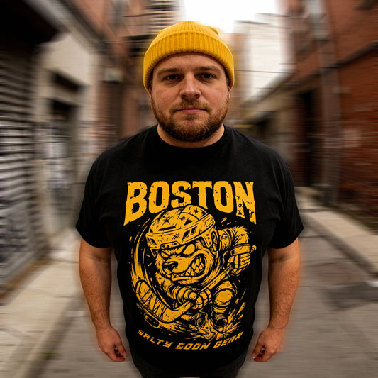 Man wearing a black t-shirt with BOTSON HOCKEY yellow graphics and text in an urban setting