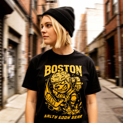 Person wearing a black t-shirt with BOTSON HOCKEY yellow graphics and text in an urban setting