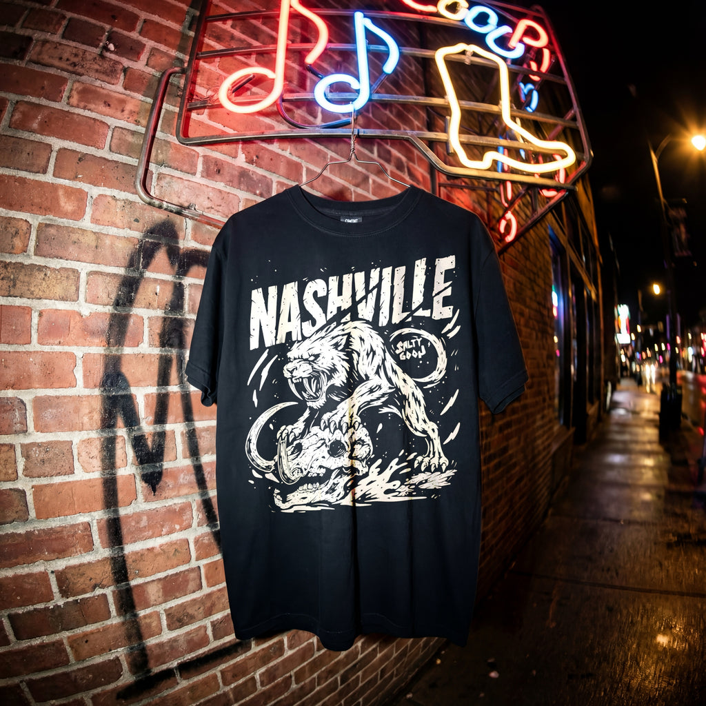 Black t-shirt with 'Nashville' design on a brick wall with neon signs in the background