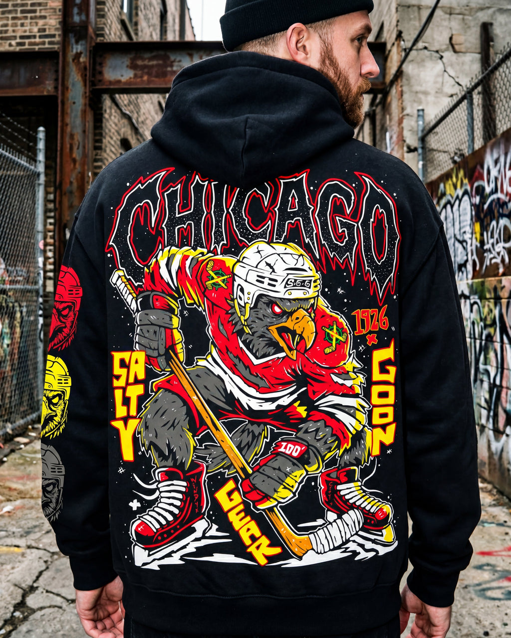 Person wearing a black hoodie with a colorful graphic design on the back, standing in an urban setting with graffiti.
