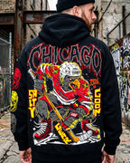 Person wearing a black hoodie with a colorful graphic design on the back, standing in an urban setting with graffiti.