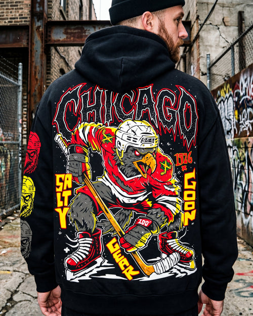 Person wearing a black hoodie with a colorful graphic design on the back, standing in an urban setting with graffiti.