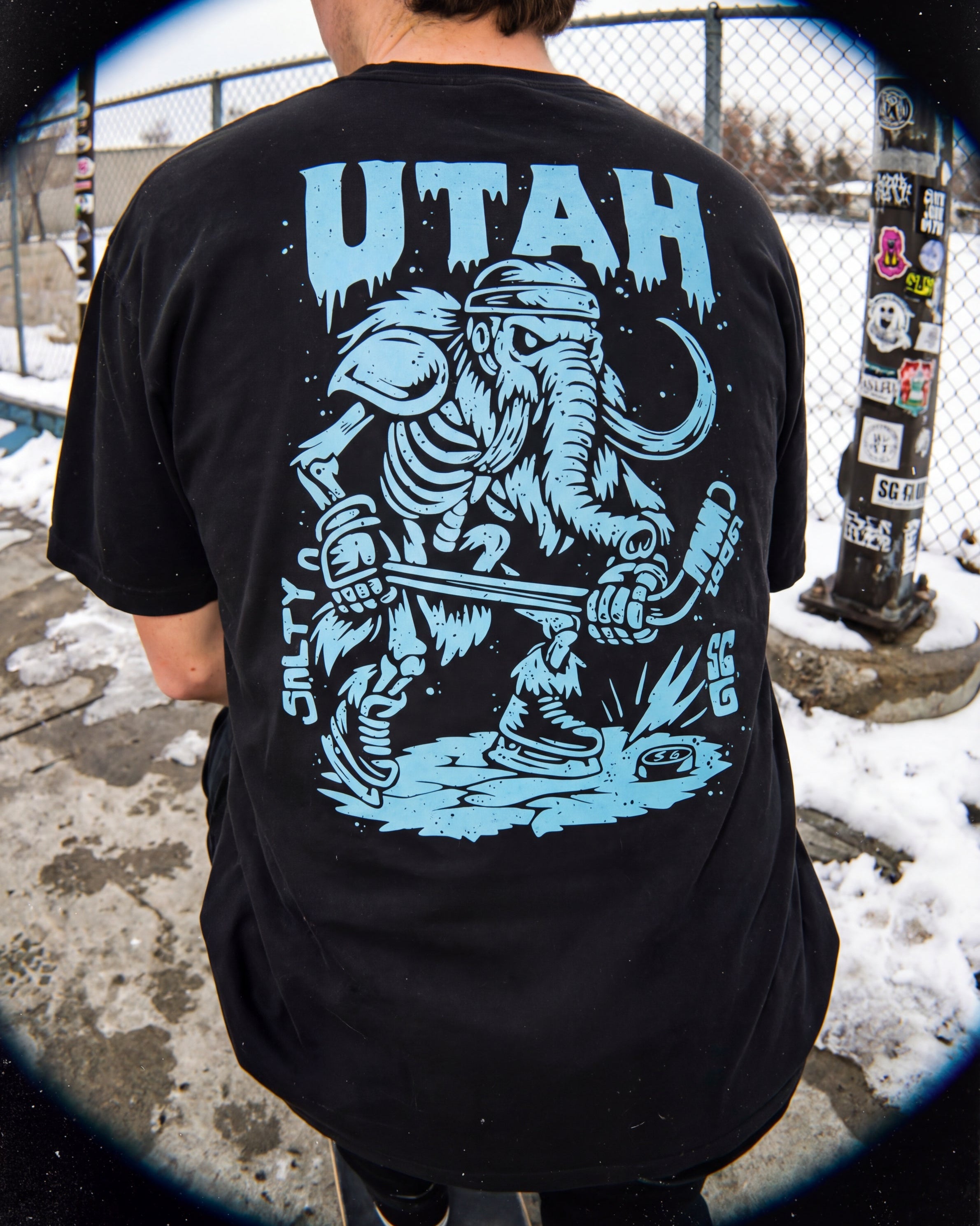 Person wearing a black t-shirt with blue 'UTAH' and graphic design outdoors.