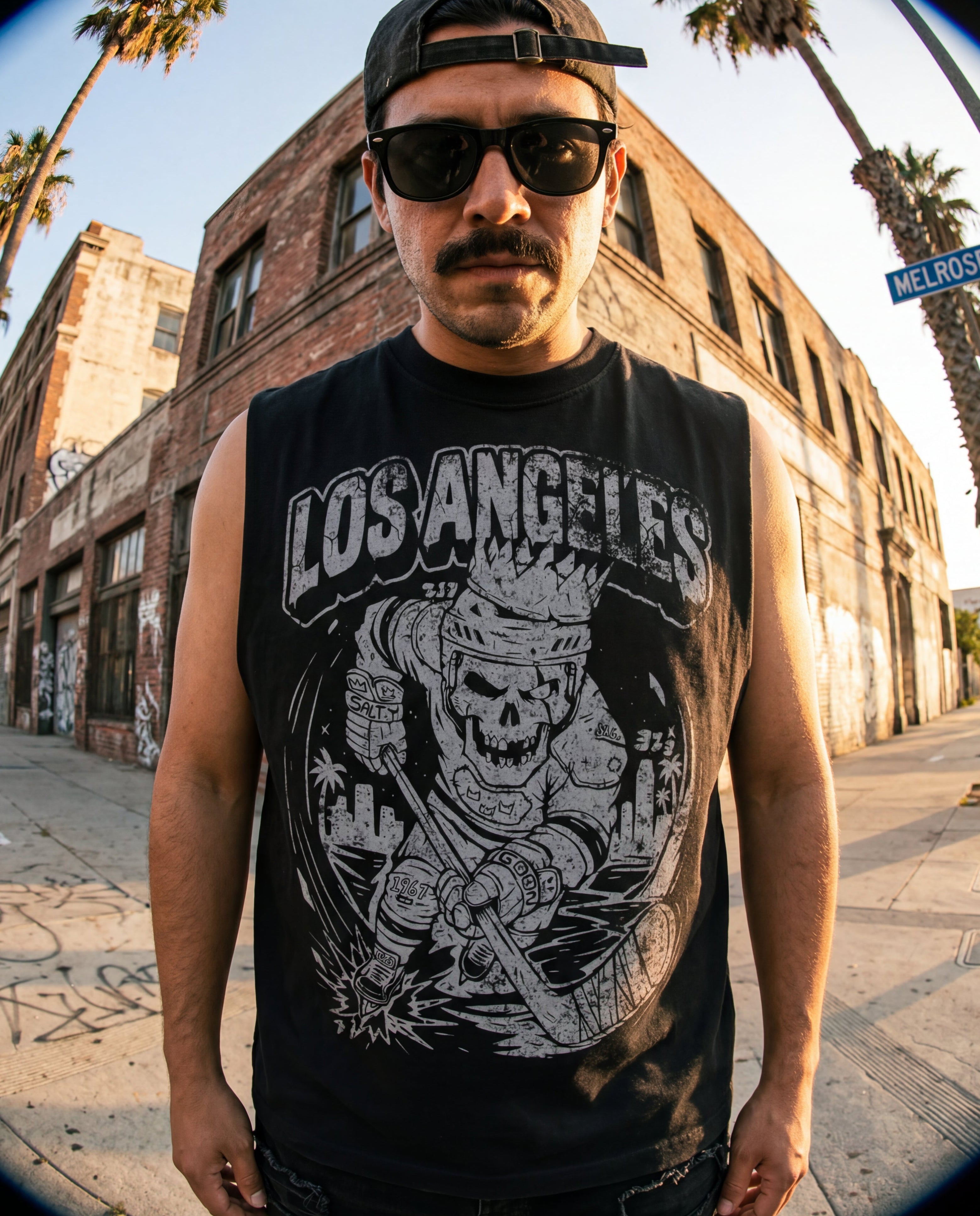 Person wearing a 'Los Angeles' sleeveless shirt with a skull design on a street with palm trees.